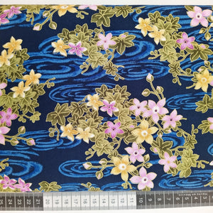 Patchwork stof, blå bund med japansk inspireret motiv med store flotte blomster og blade i grøn, lyserød og gul farver alt er optegner med guld.