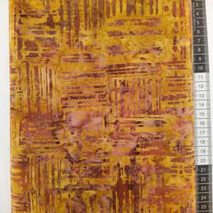 Patchwork stof, gylden gul/brun med lilla streger der skaber et flot mønster.